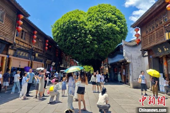 7月8日，福建福州，游客在三坊七巷古街区网红爱心树下留影。中新社记者 王东明 摄